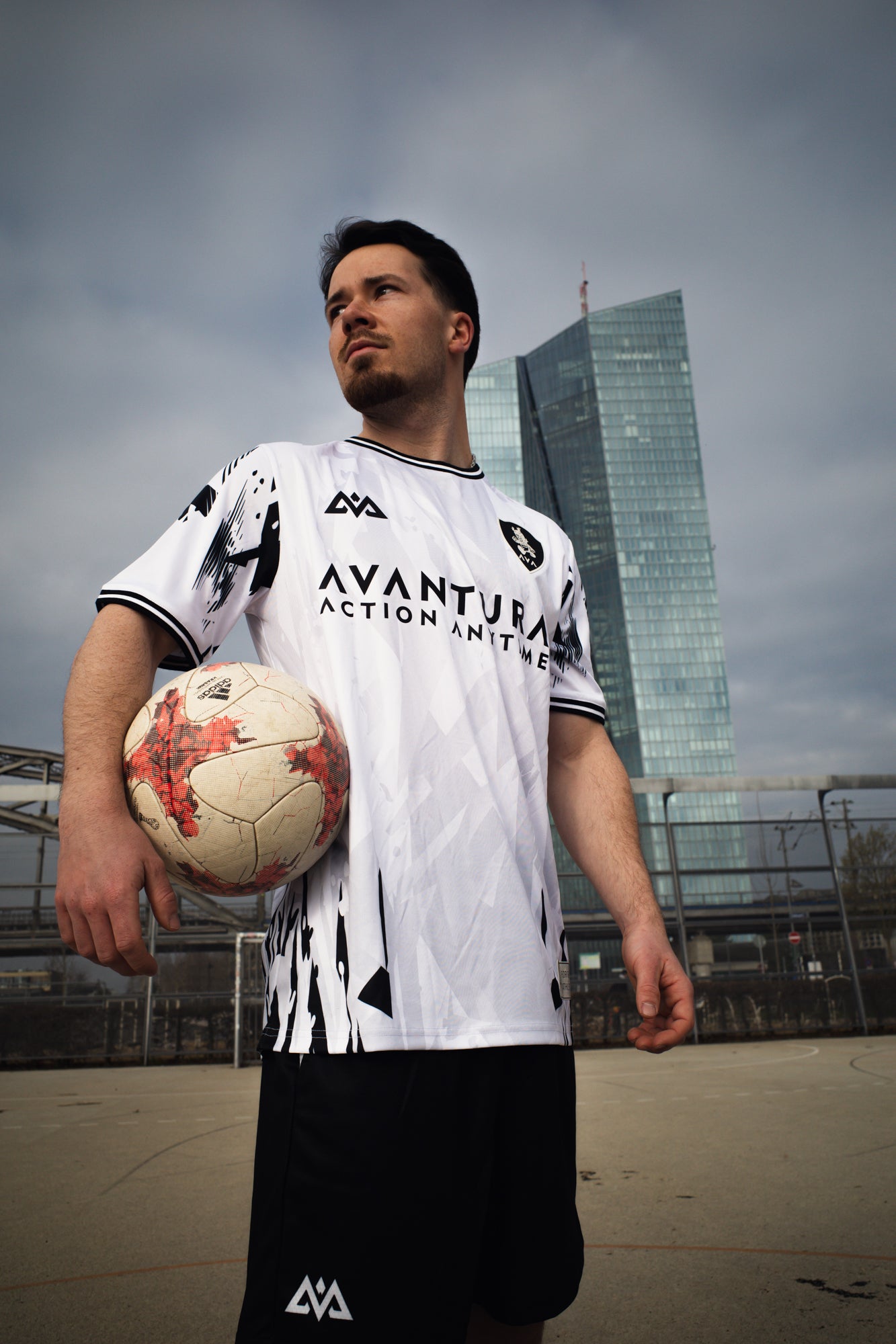 Full body view of white Avantura sports jersey and black shorts on outdoor court with urban background