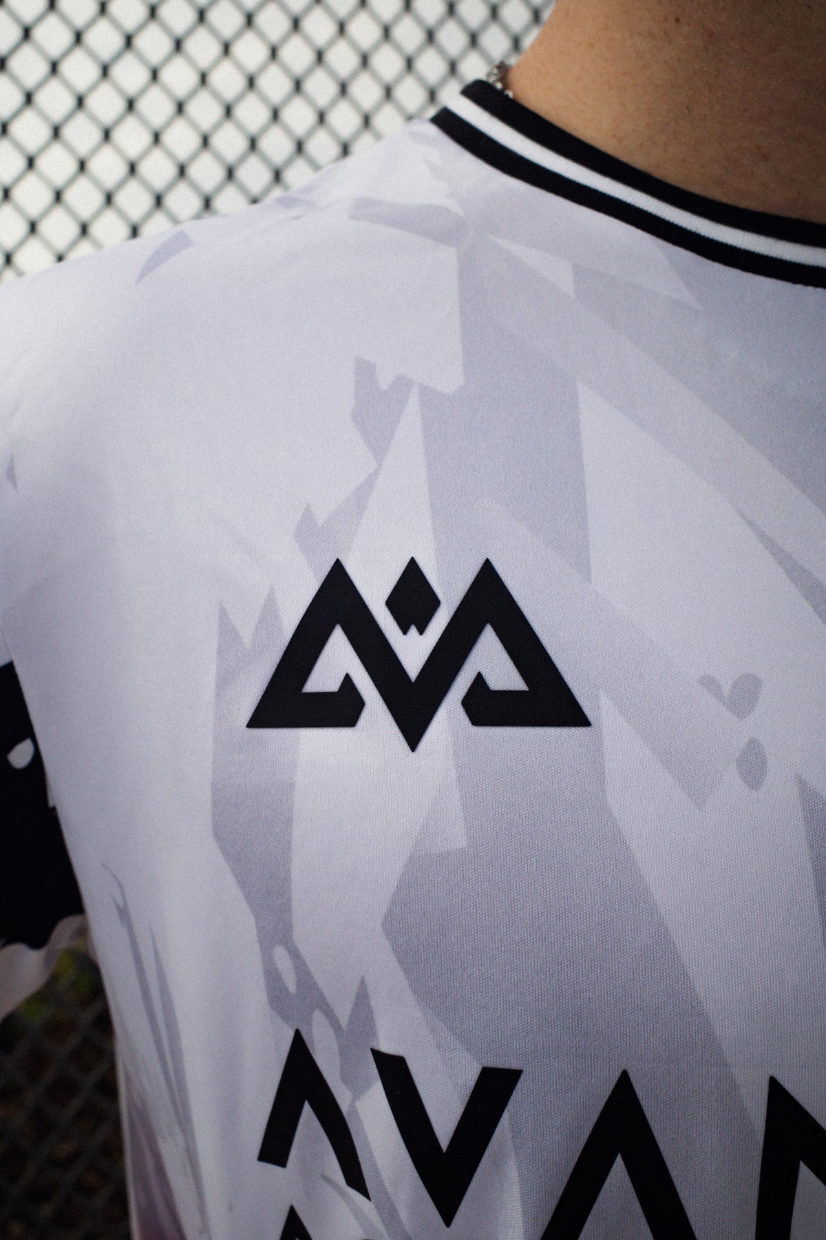 Upper back detail of white Avantura jersey showing subtle grey geometric pattern and angular logo