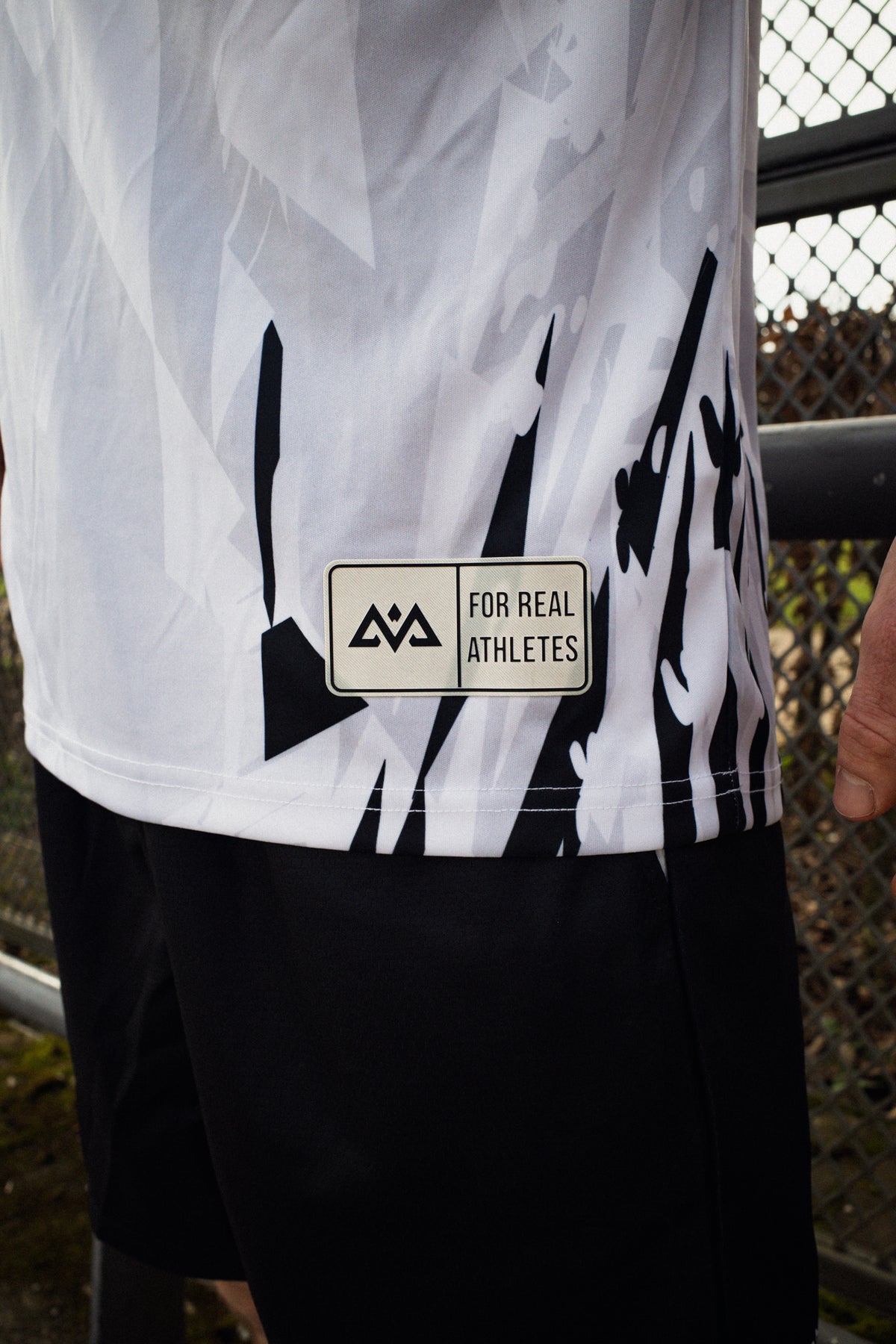 Close-up of beige woven label reading 'For Real Athletes' on white Avantura jersey side hem