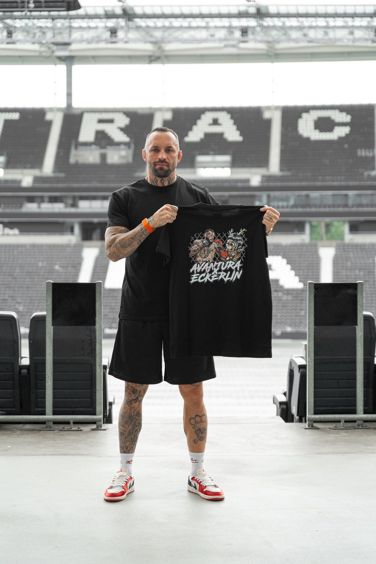 Tätowierter Mann präsentiert schwarzes T-Shirt mit großem Rückendesign