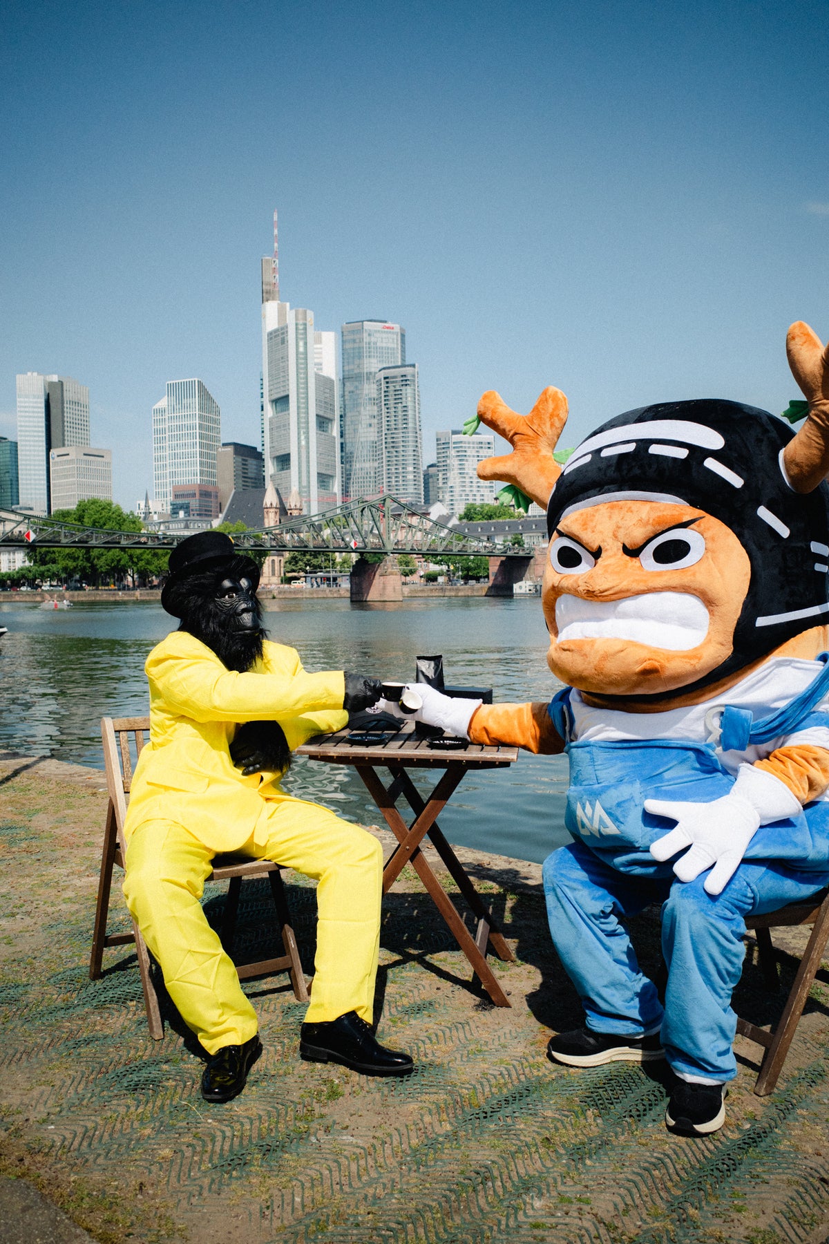Lifestyle shot of black t-shirt wearer sitting at table with gorilla mascot in city park