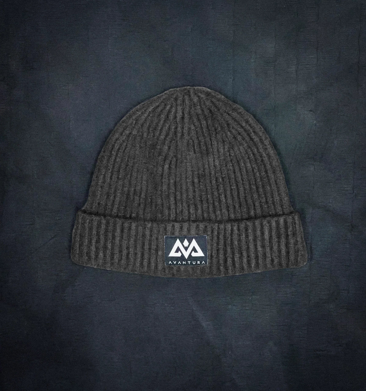 Dark gray ribbed knit beanie with folded cuff and woven AVANTURA patch logo