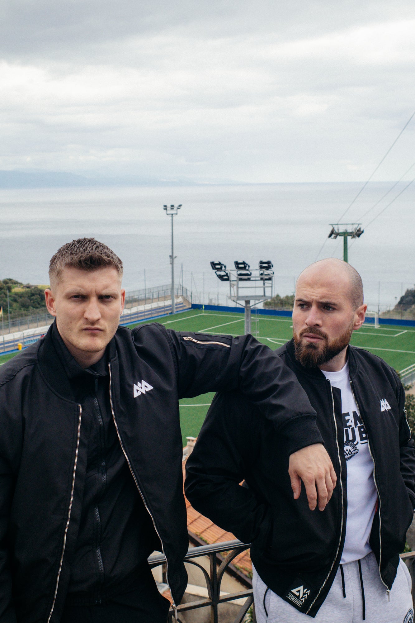 Men wearing black bomber jackets with white chest logo on balcony
