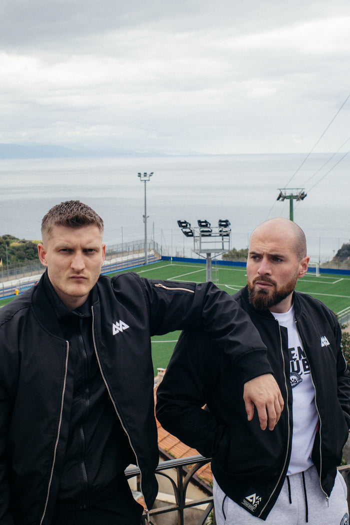Men wearing black bomber jackets with white chest logo on balcony