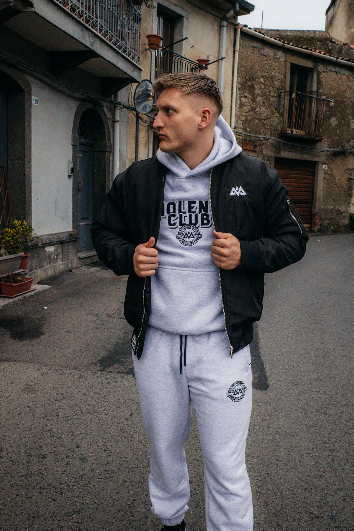 Man styling black bomber jacket over grey hoodie