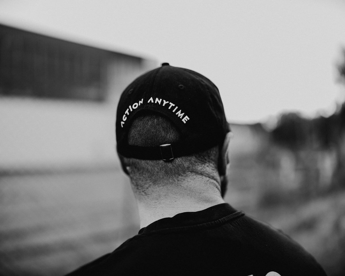 Back view of black cap showing 'ACTION ANYTIME' text and adjustable strap