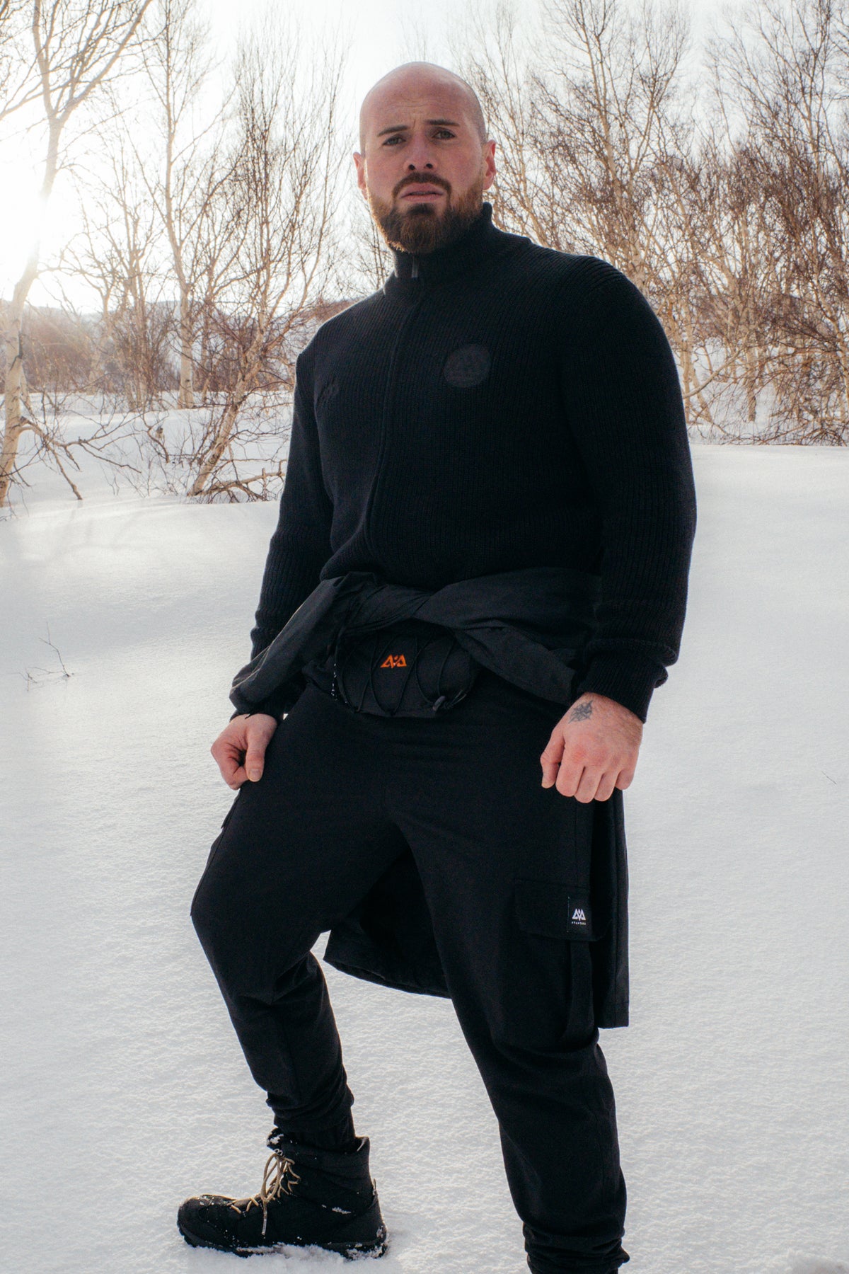 Mann in schwarzer Cargohose, Pullover und Gürtel im Schnee
