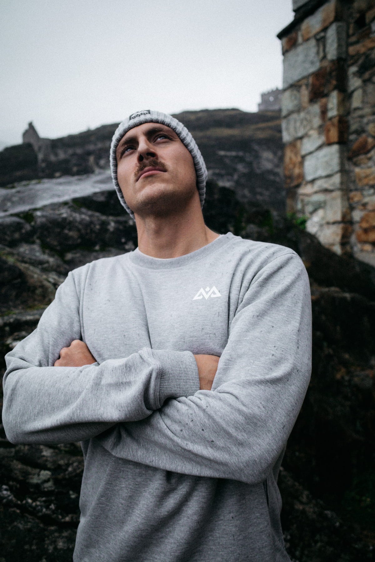 Mann trägt grauen Crewneck Sweater mit Logo vor historischem Hintergrund