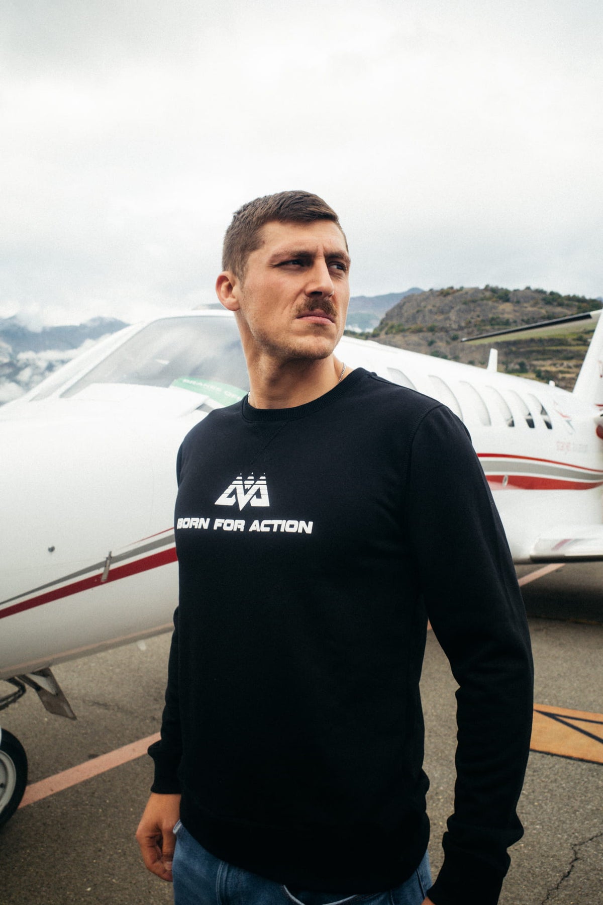 Schwarzer Crewneck Sweatshirt mit weißem Logo vor Flugzeug