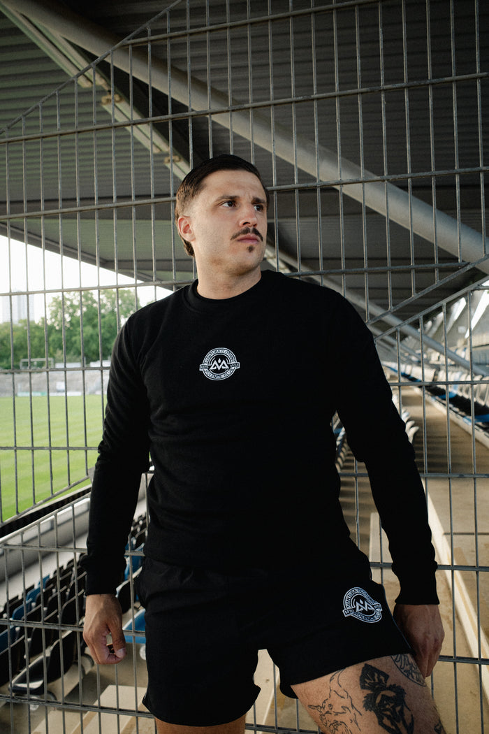 Man wearing black crewneck sweater and matching shorts at stadium