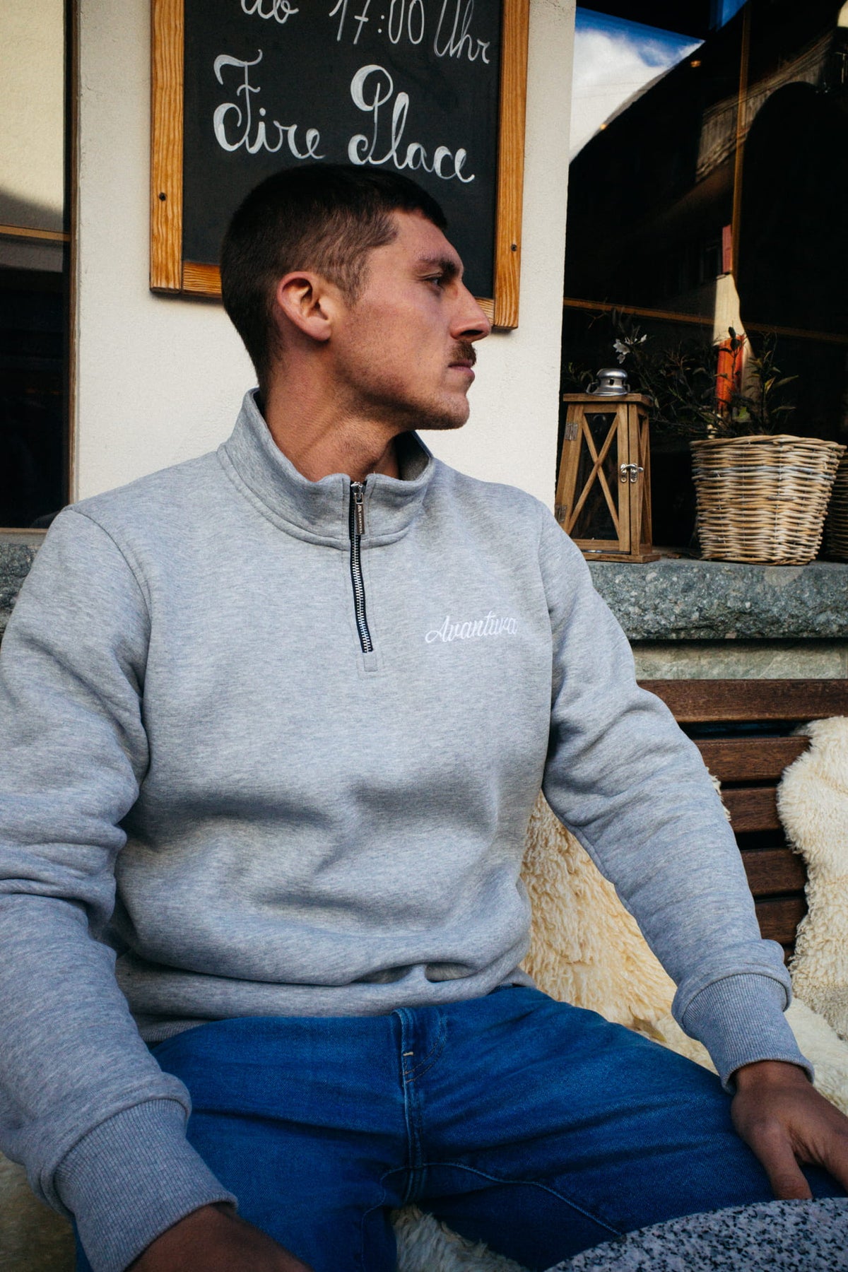 Light gray half-zip sweater with embroidery, sitting on a wooden bench
