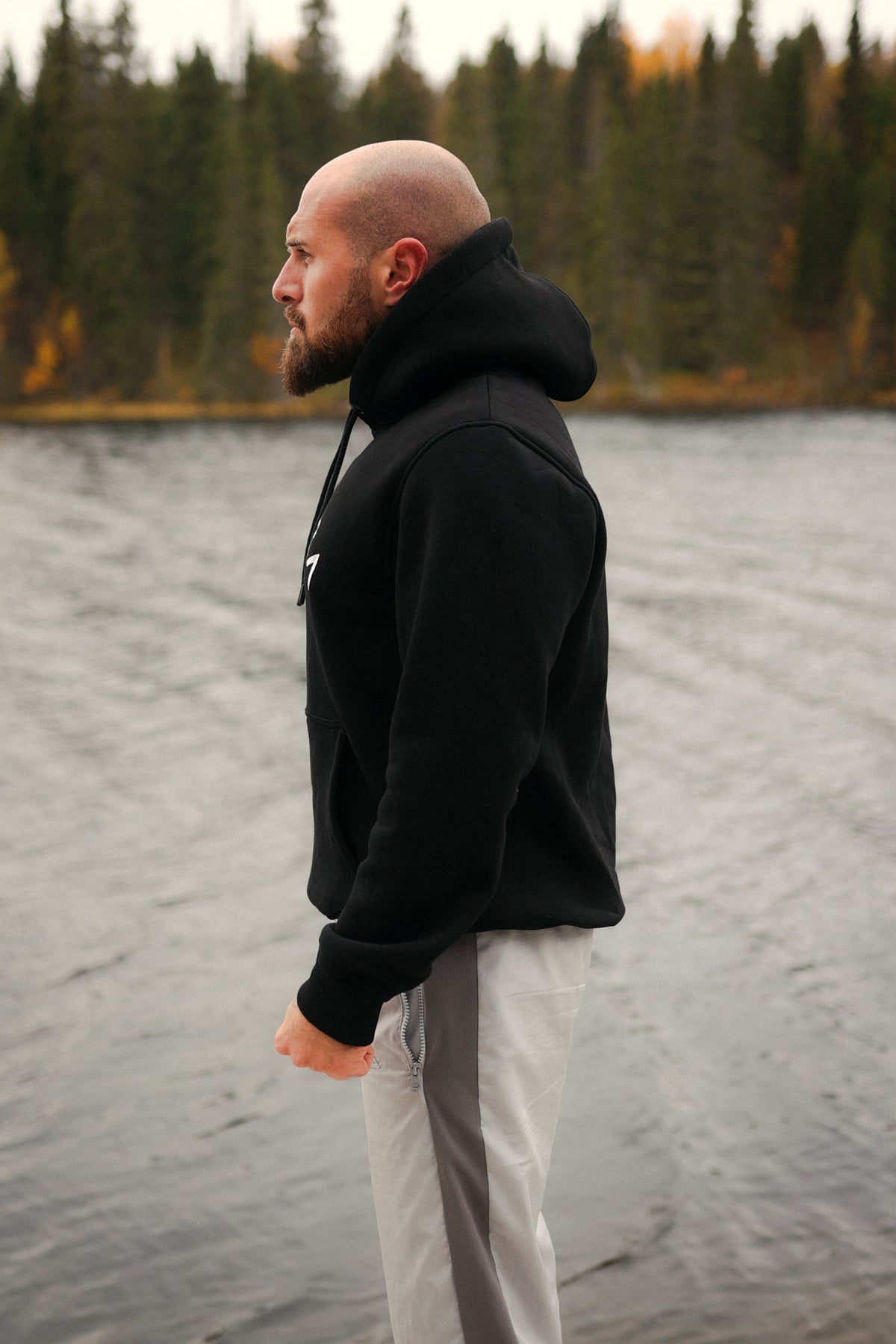 Seitenansicht des schwarzen Avantura Hoodies mit Kapuze am Wasser