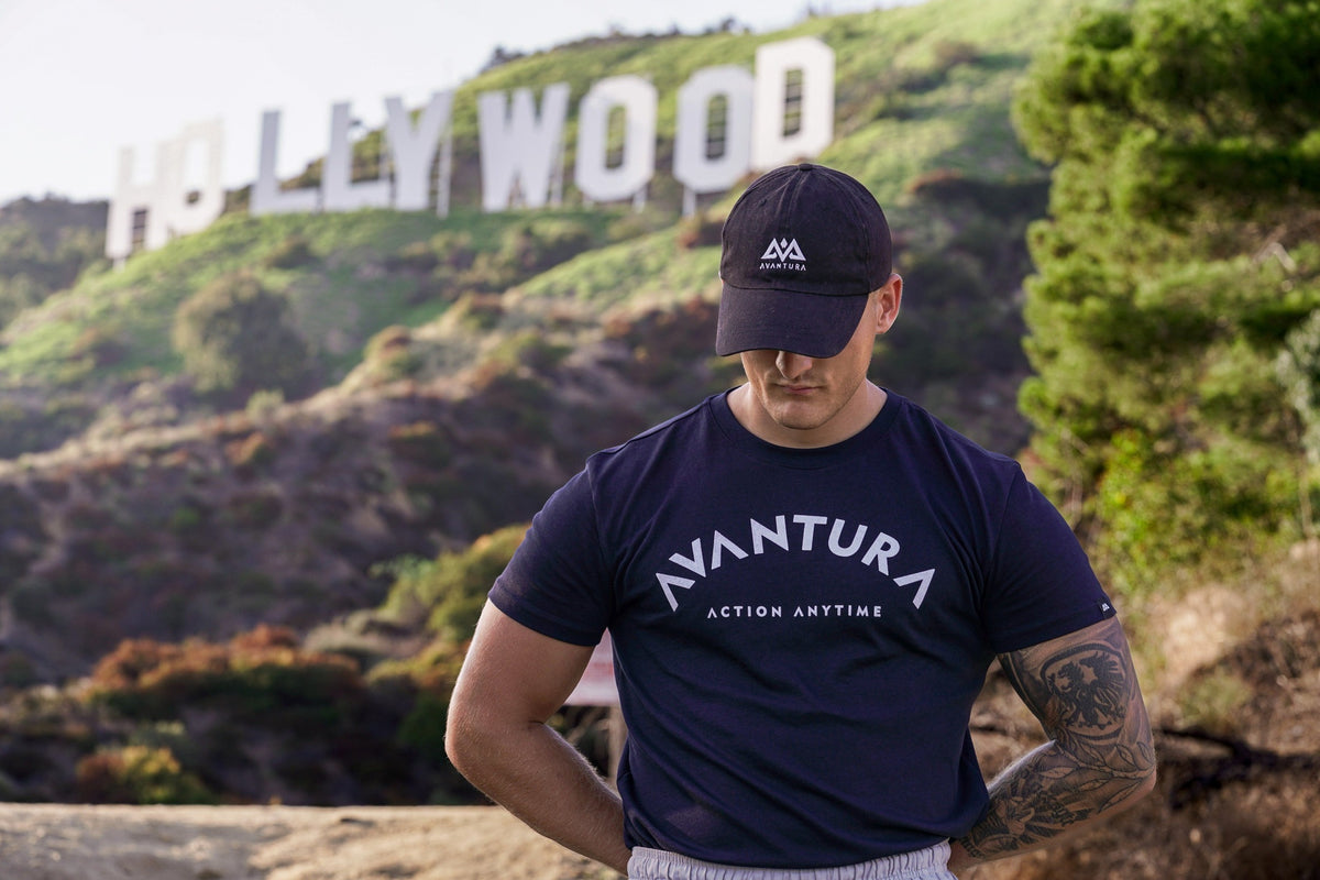 Mann trägt dunkelblaues T-Shirt mit gebogenem Schriftzug vor Hollywood Schild