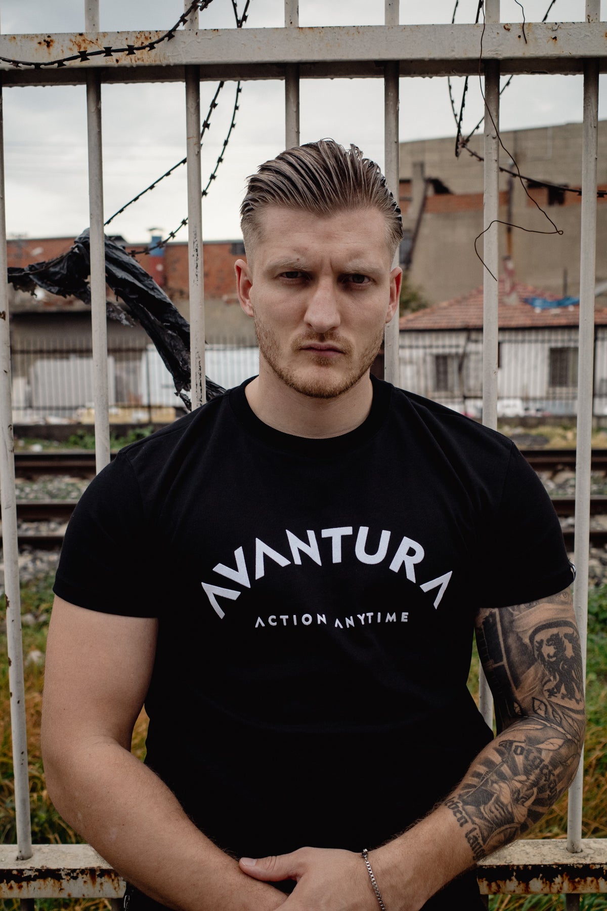 Front view of black T-shirt featuring arched 'AVANTURA' graphic and 'ACTION ANYTIME' slogan