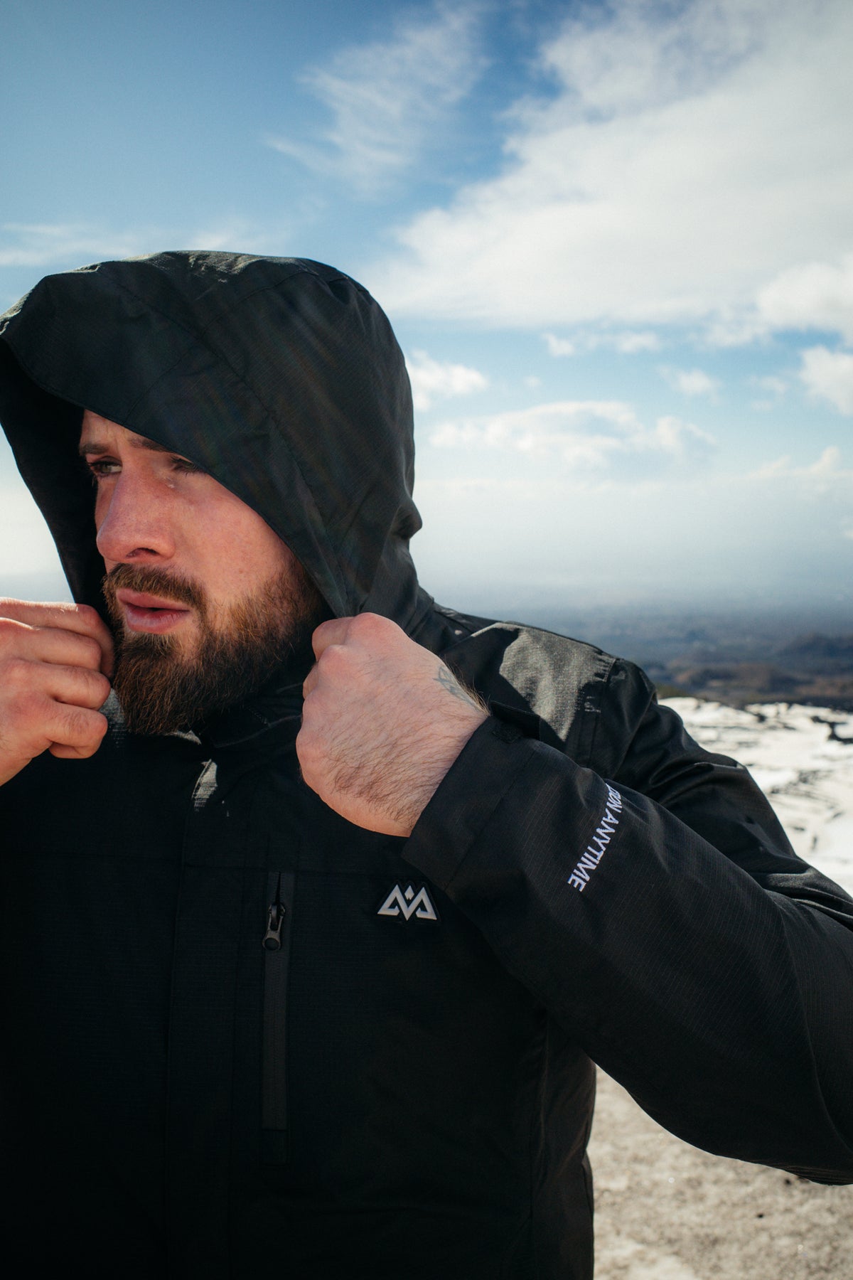 Close-up of black hooded jacket collar and chest logo on bearded man