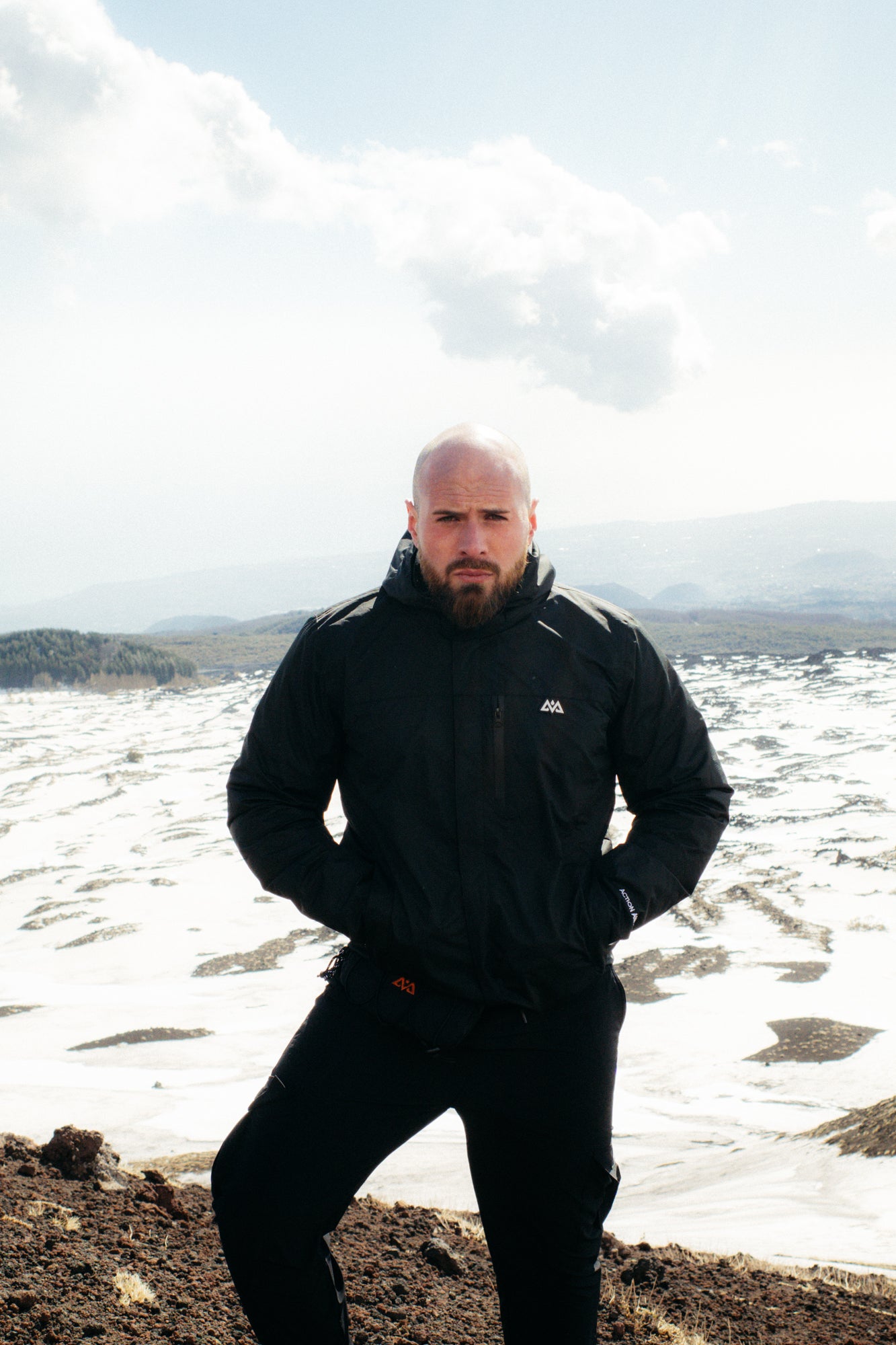 Front view of black rain jacket with hands in pockets on rocky outcrop