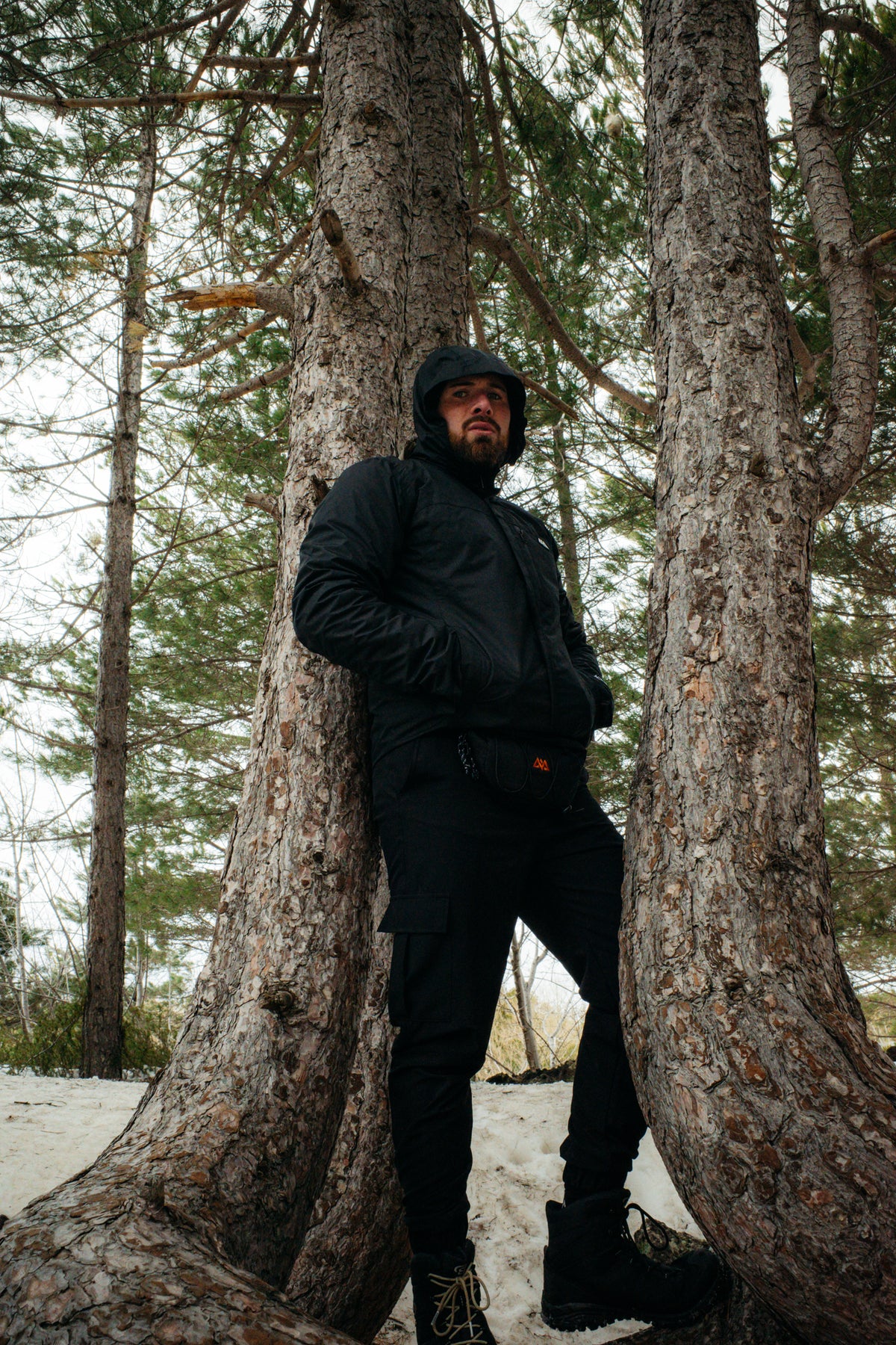 Man wearing black hooded rain jacket and cargo pants in snowy forest