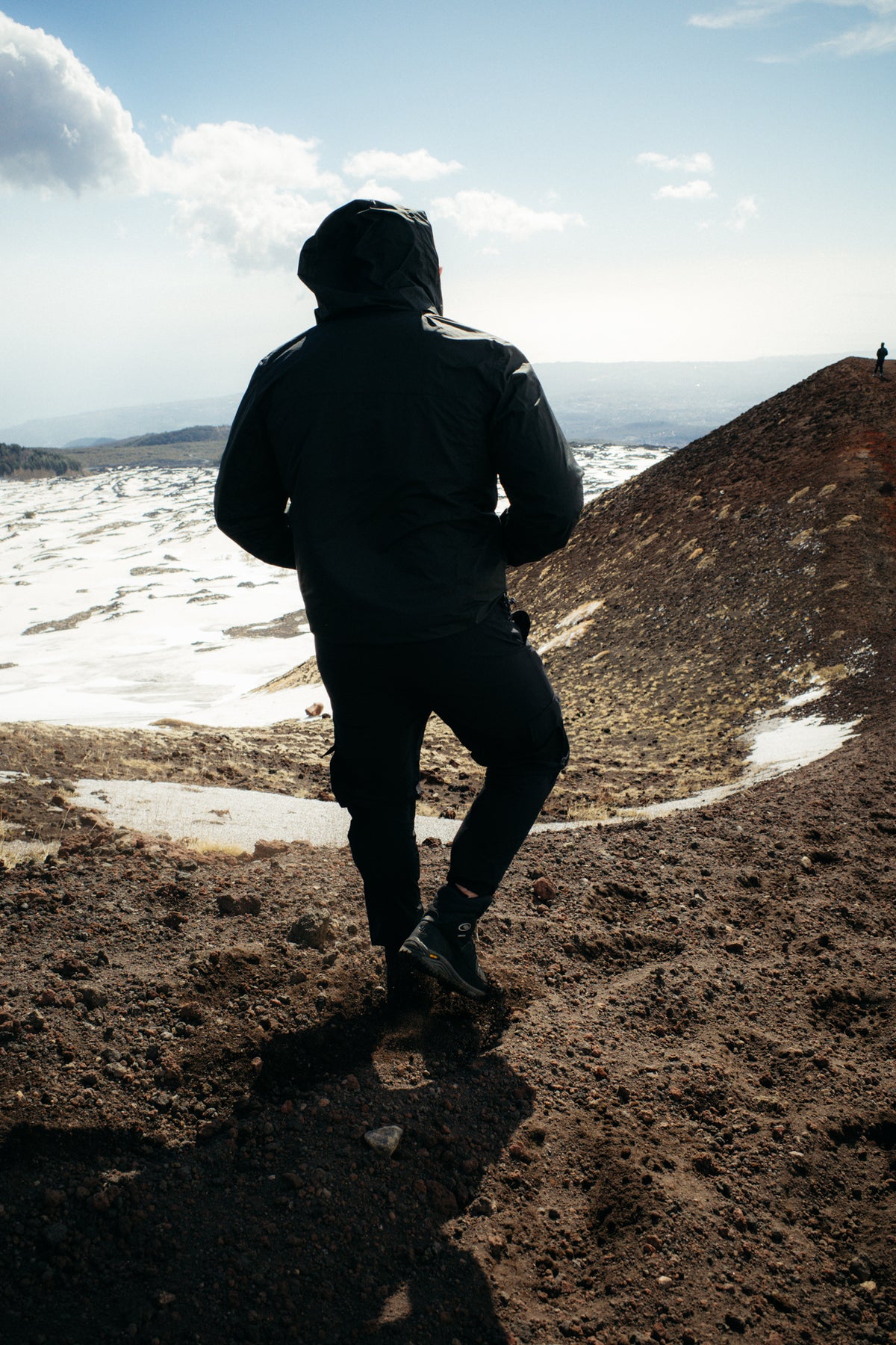 Rear view of black technical rain jacket worn hiking uphill in snow