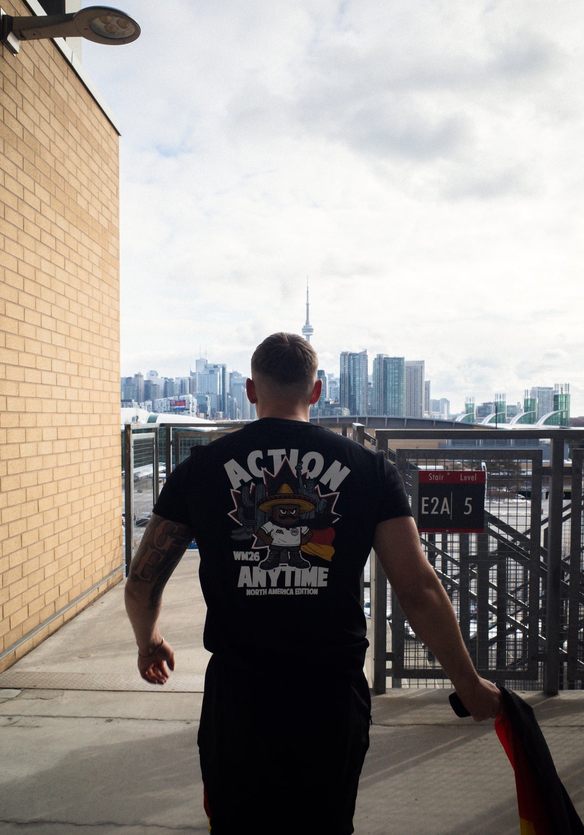 Man walking outdoors holding German flag while wearing graphic black T-shirt
