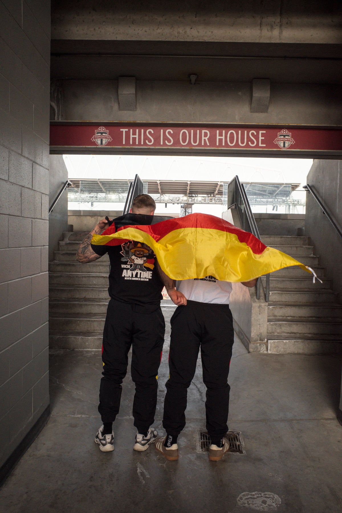 German flag held by two men wearing black and white T-shirts in stadium