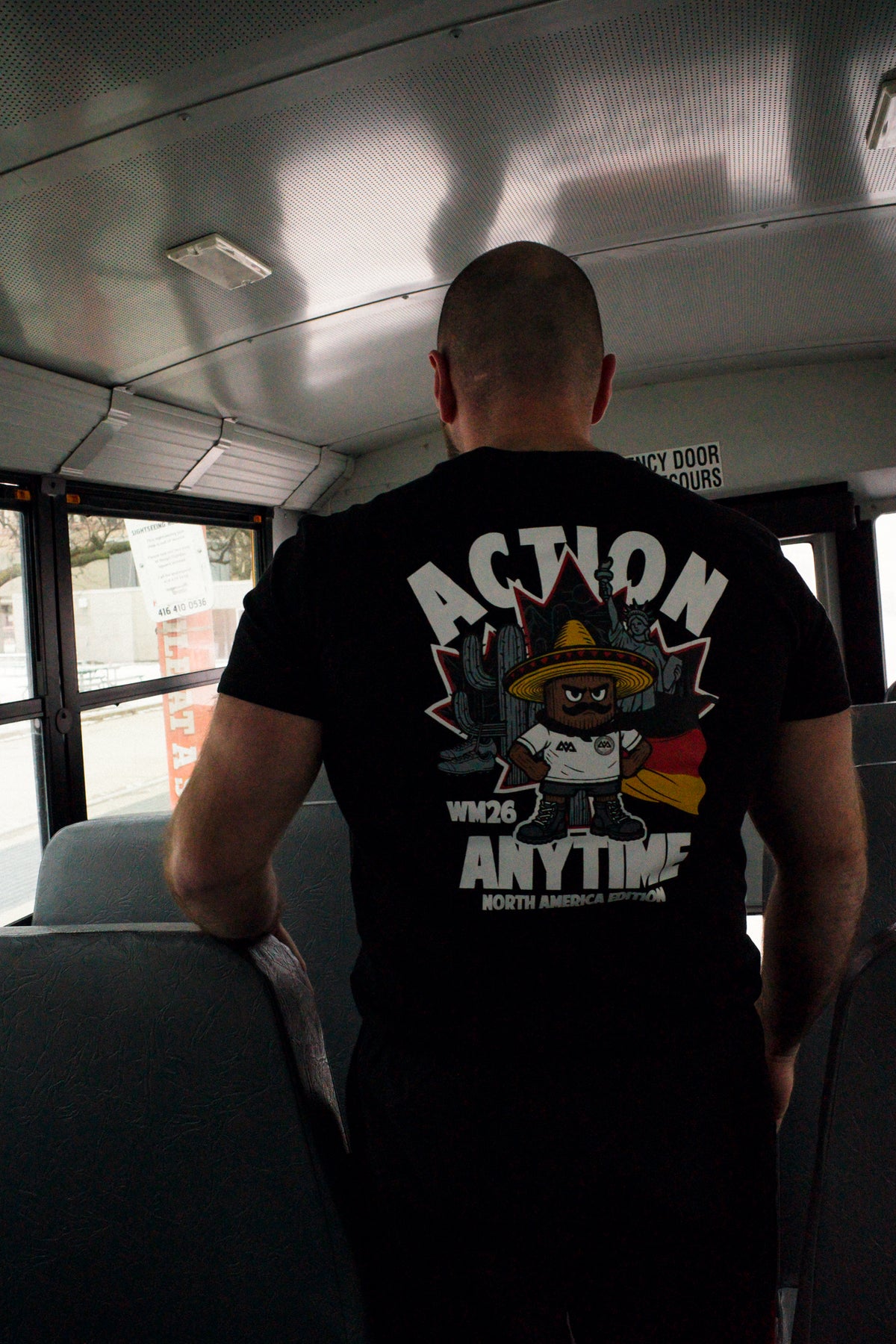 Man on bus wearing black T-shirt with large Action Anytime back print