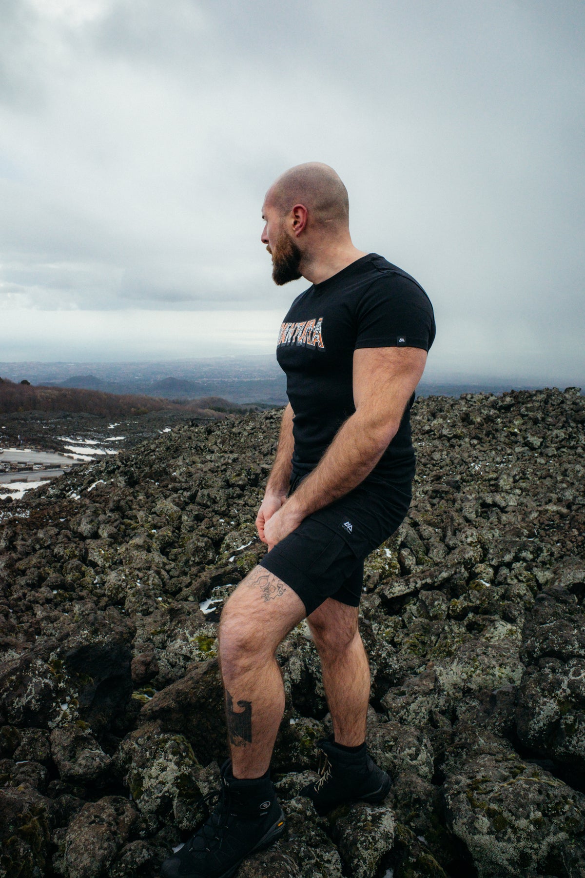 Man wearing black Avantura t-shirt and shorts in rugged outdoor setting