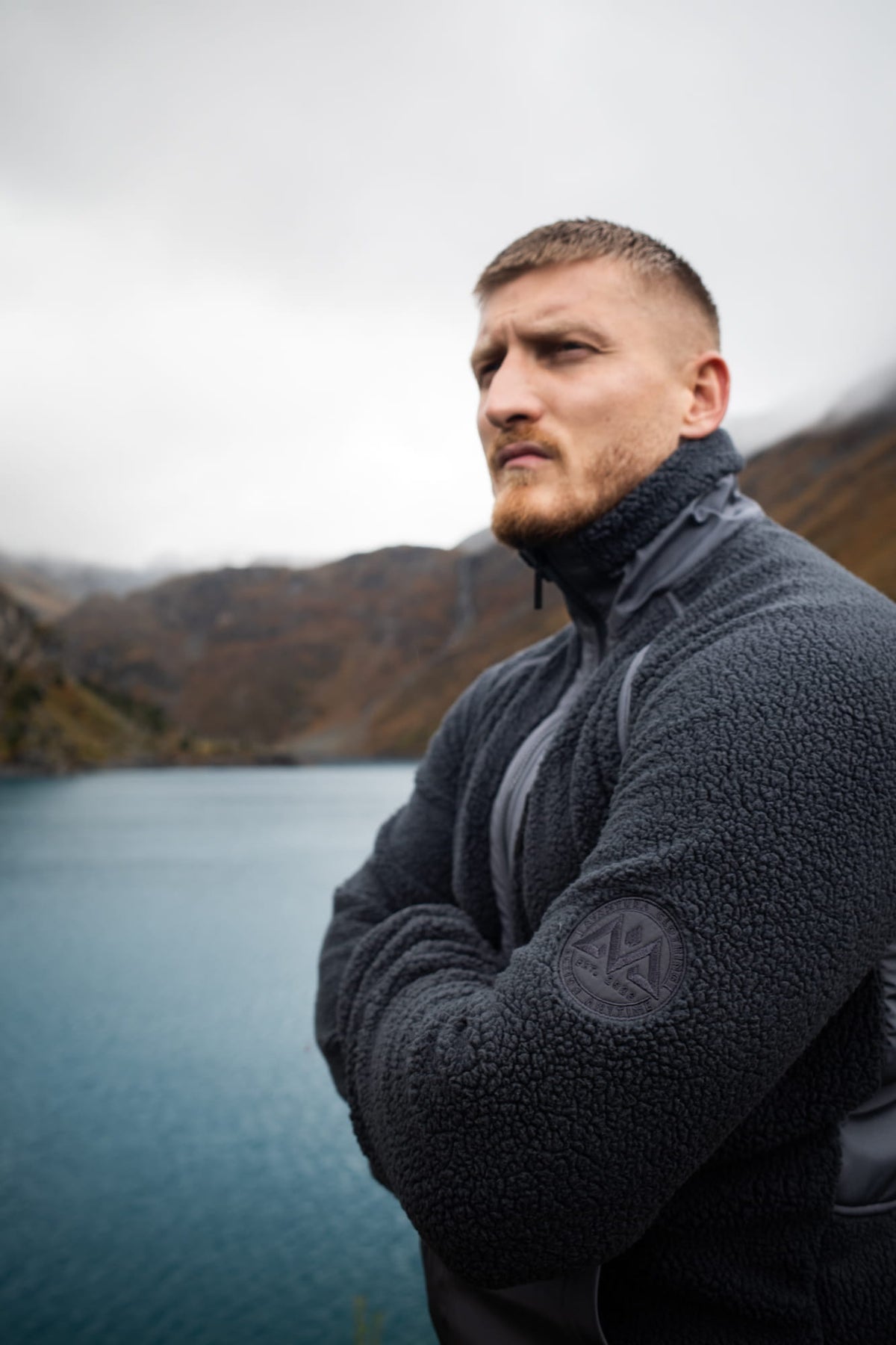 Graue Fleecejacke mit kreisförmigem Logopatch vor Bergpanorama