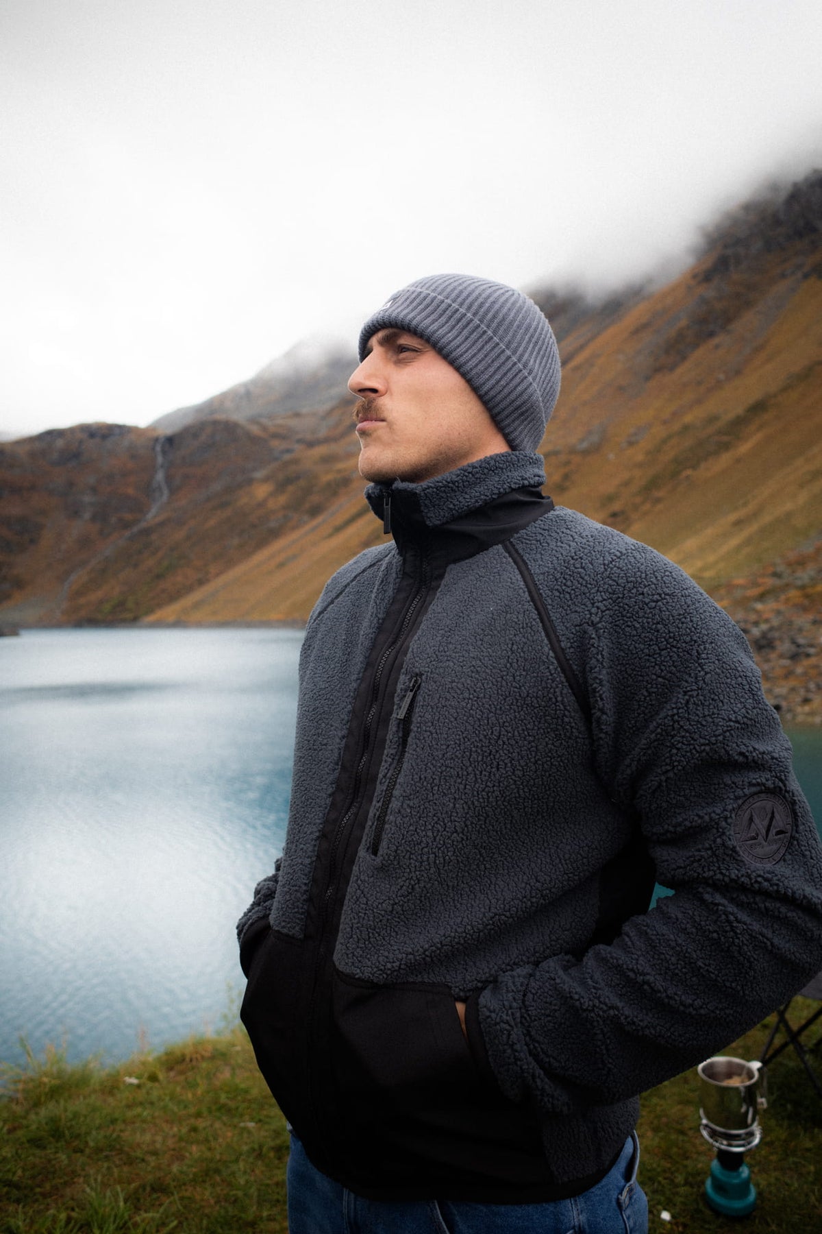 Grau-schwarze Fleecejacke mit Logopatch am Arm, getragen in Berglandschaft