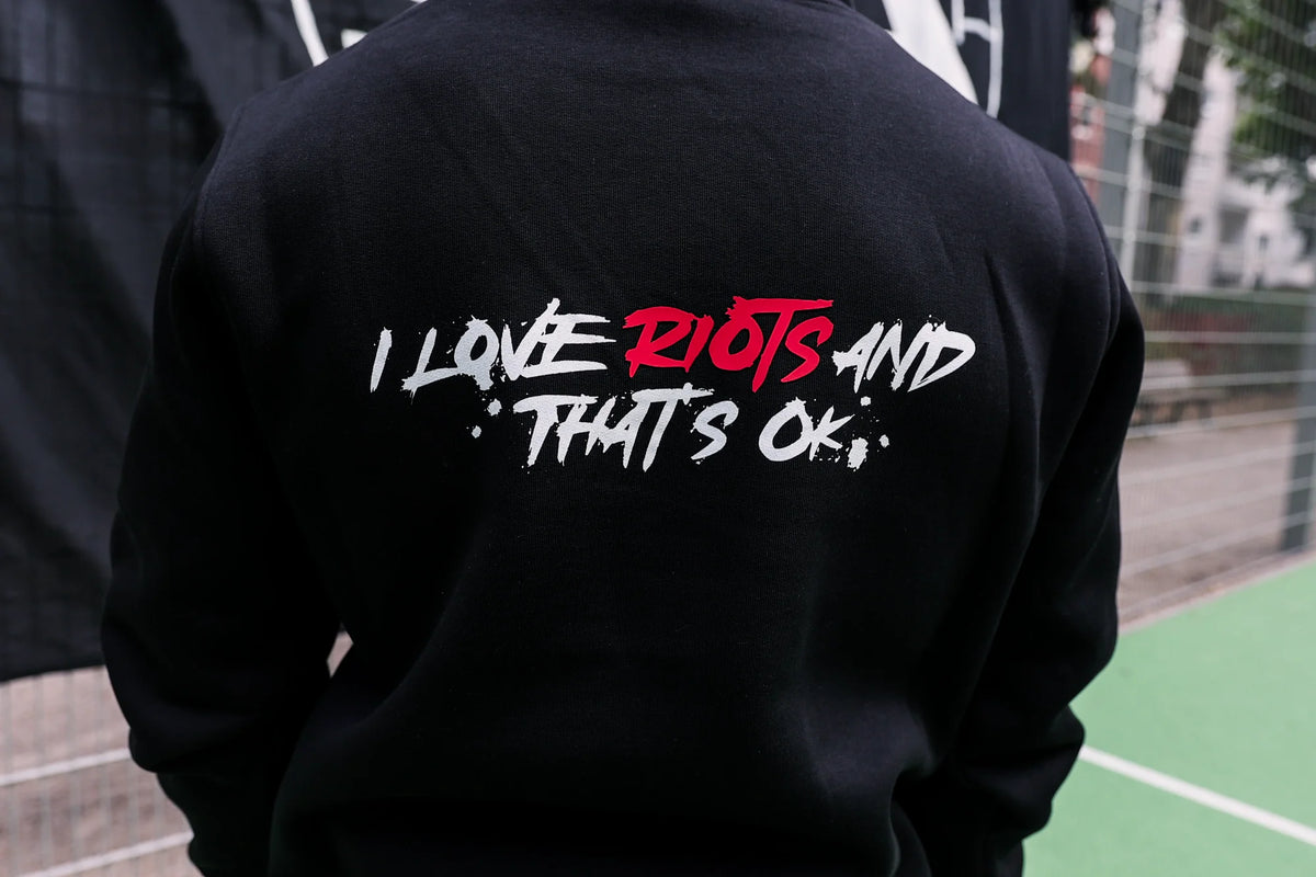 Black hoodie back view featuring large 'I LOVE RIOTS' brush stroke graphic in white and red