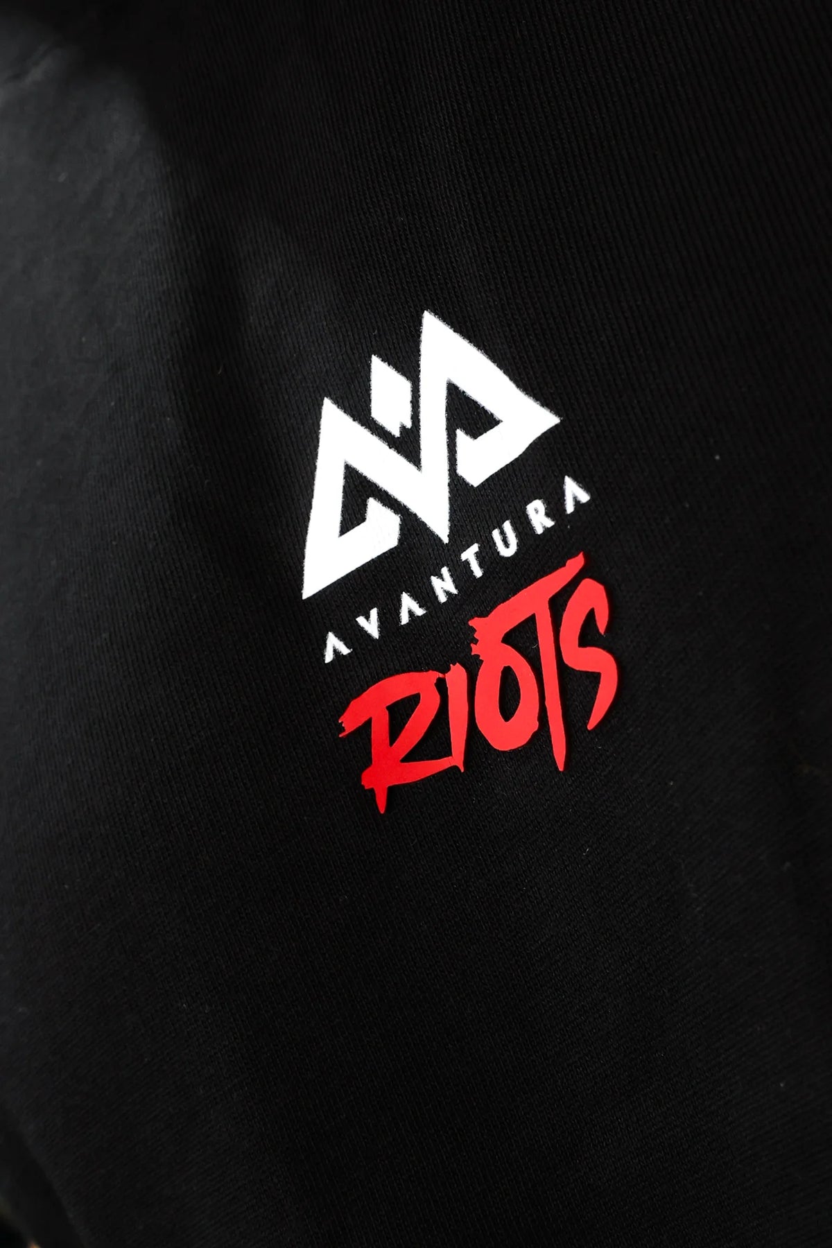Close-up of Avantura logo on black t-shirt chest featuring geometric symbol and red text