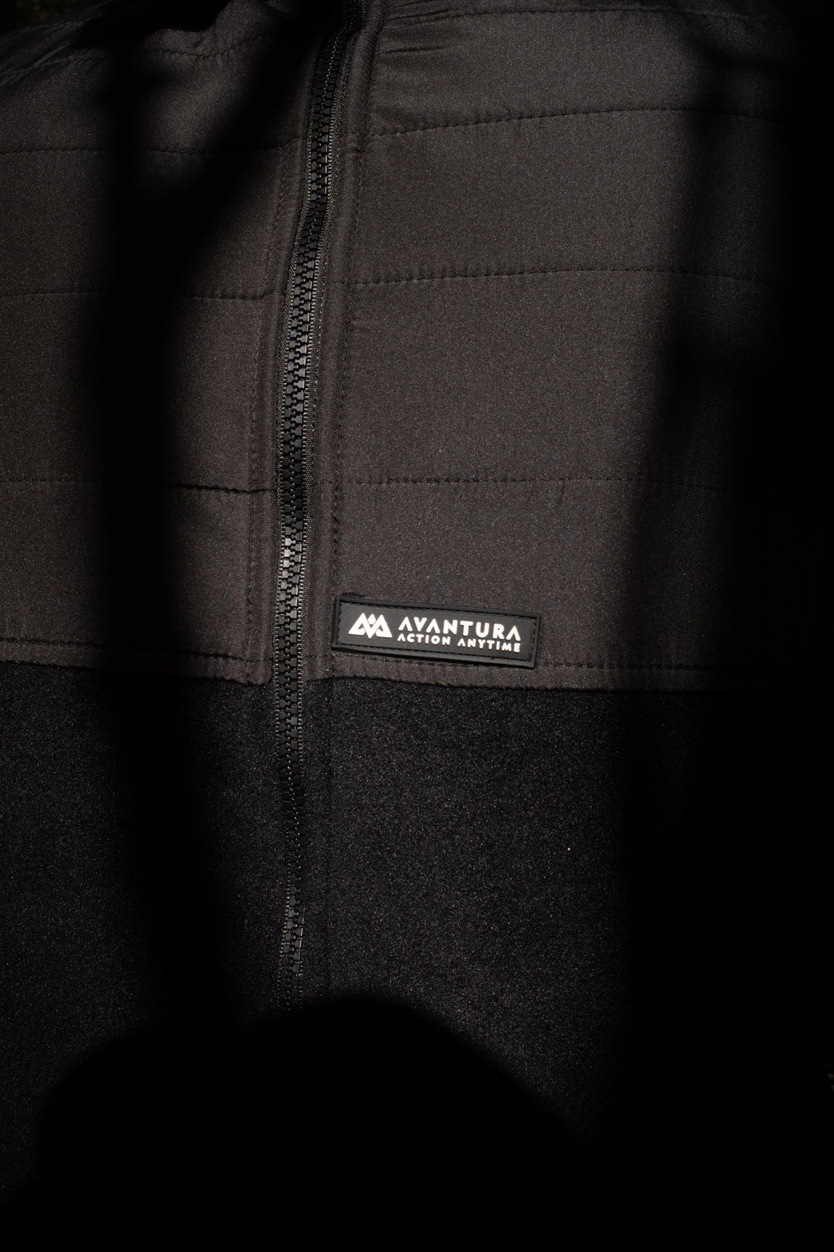 Detail shot of black fleece jacket zipper, quilted chest, and ACTION ANYTIME label