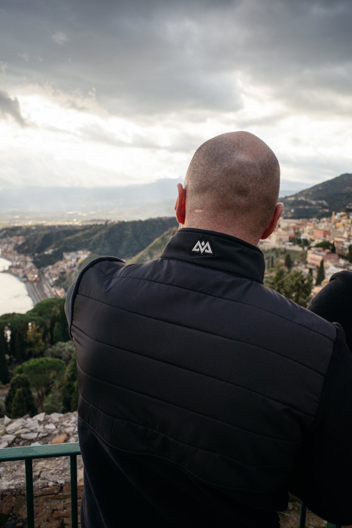Man wearing black fleece jacket overlooking coastal town, showing back quilting detail