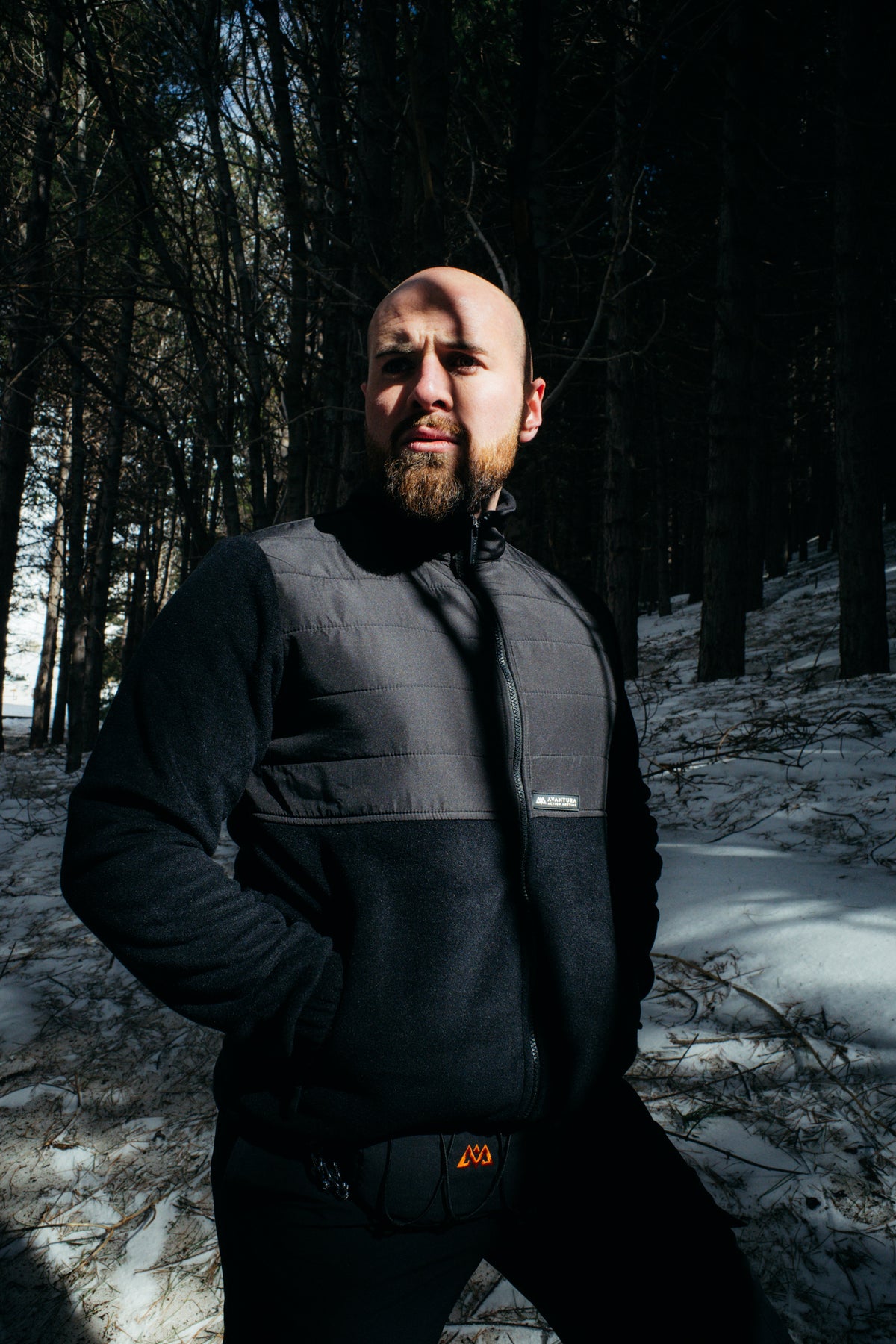 Man in black two-tone fleece jacket with hands in pockets in snowy woods