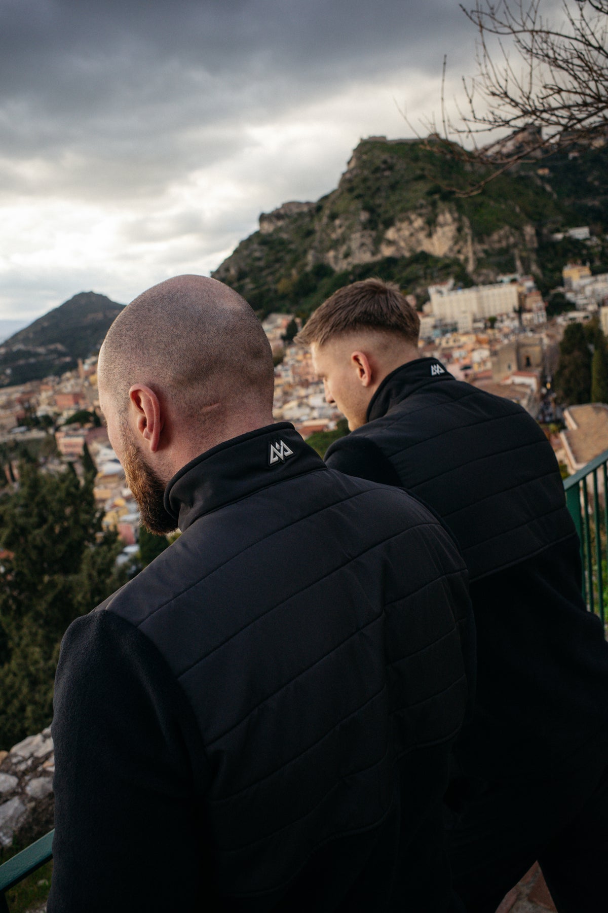 Two men in black fleece jackets standing together, displaying back collar logos