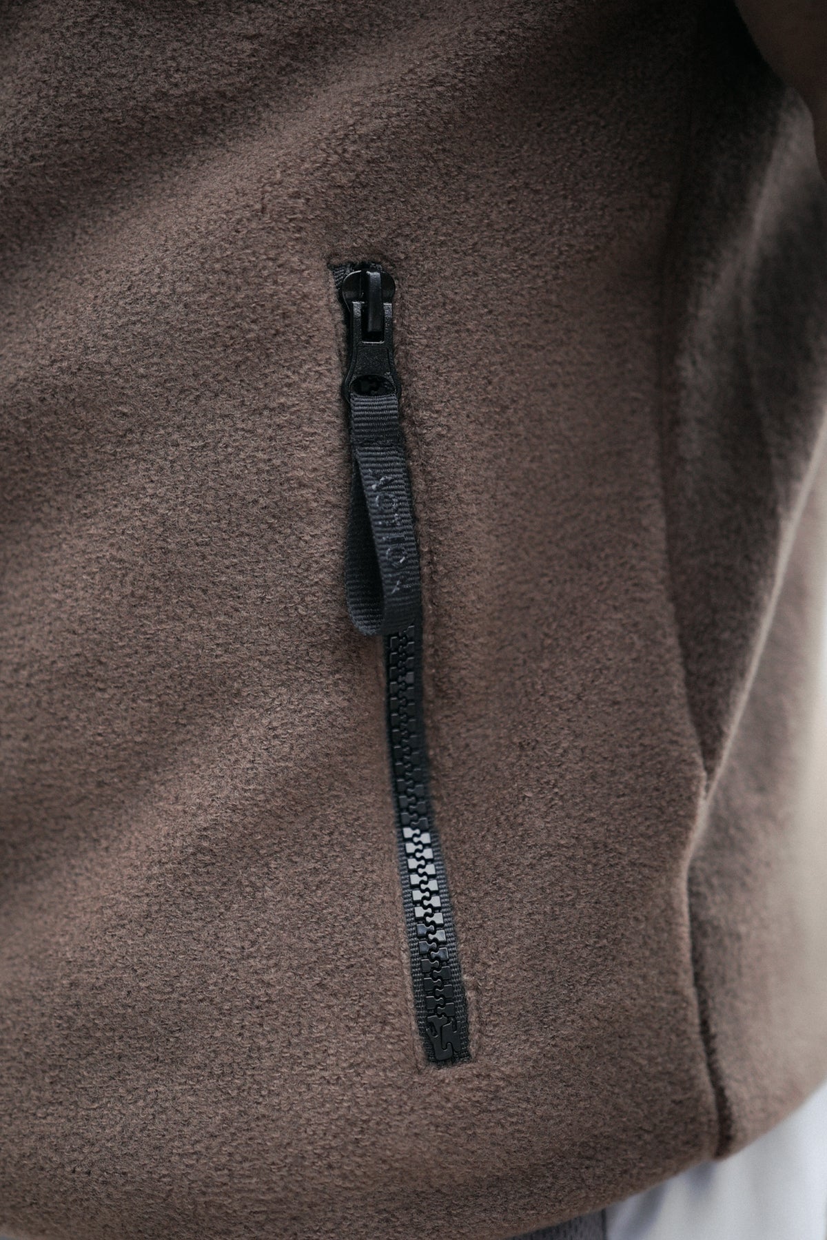 Close-up of black 'ACTION' branded zipper pull on brown fleece