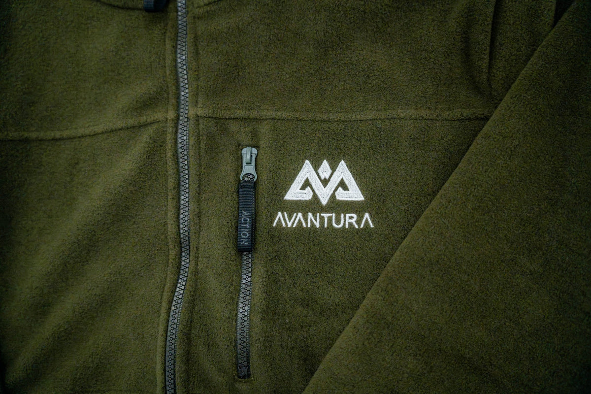 Left chest detail of olive green fleece jacket showing zippered pocket and logo
