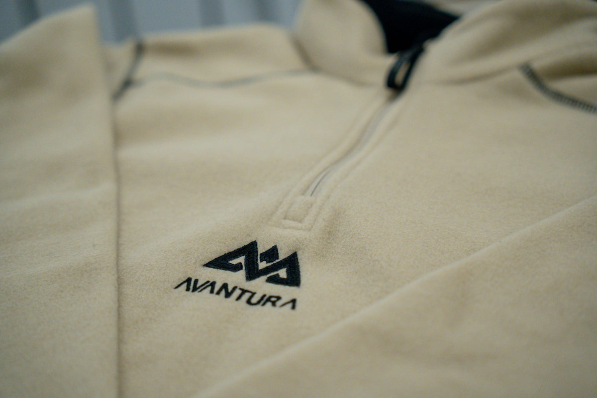 Close-up of embroidered AVANTURA logo on beige fleece fabric