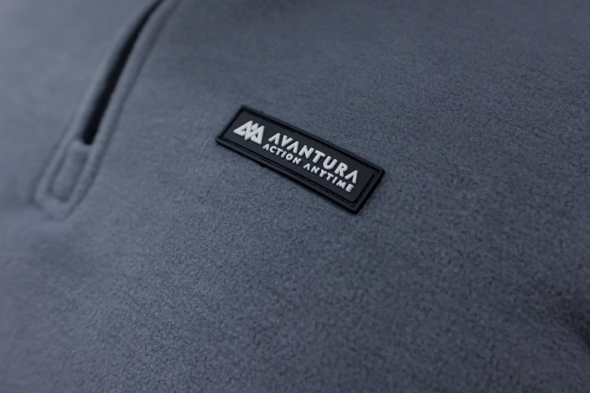 Grey halfzip fleece sweater fabric texture with embossed AVANTURA logo patch and zipper detail