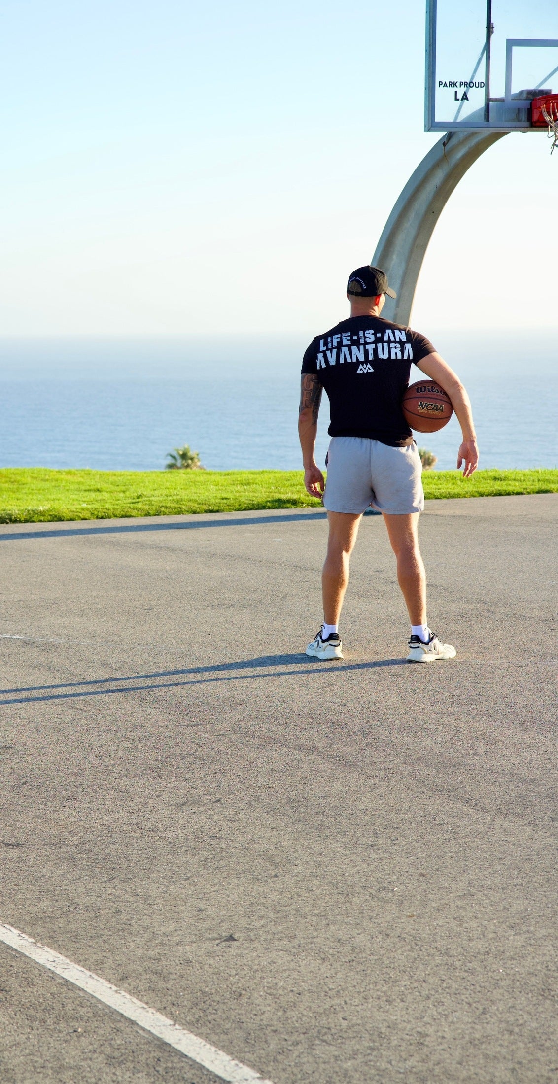 Man wearing black Avantura t-shirt with white back print on basketball court