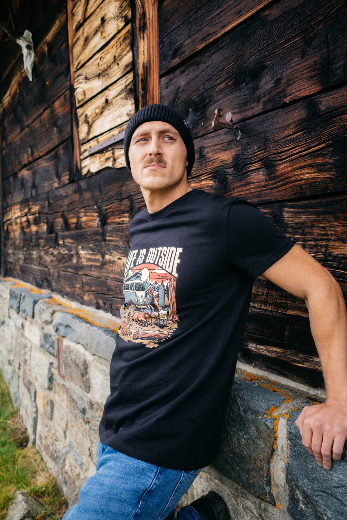Schwarzes T-Shirt mit LIFE IS OUTSIDE Grafik an Holzwand