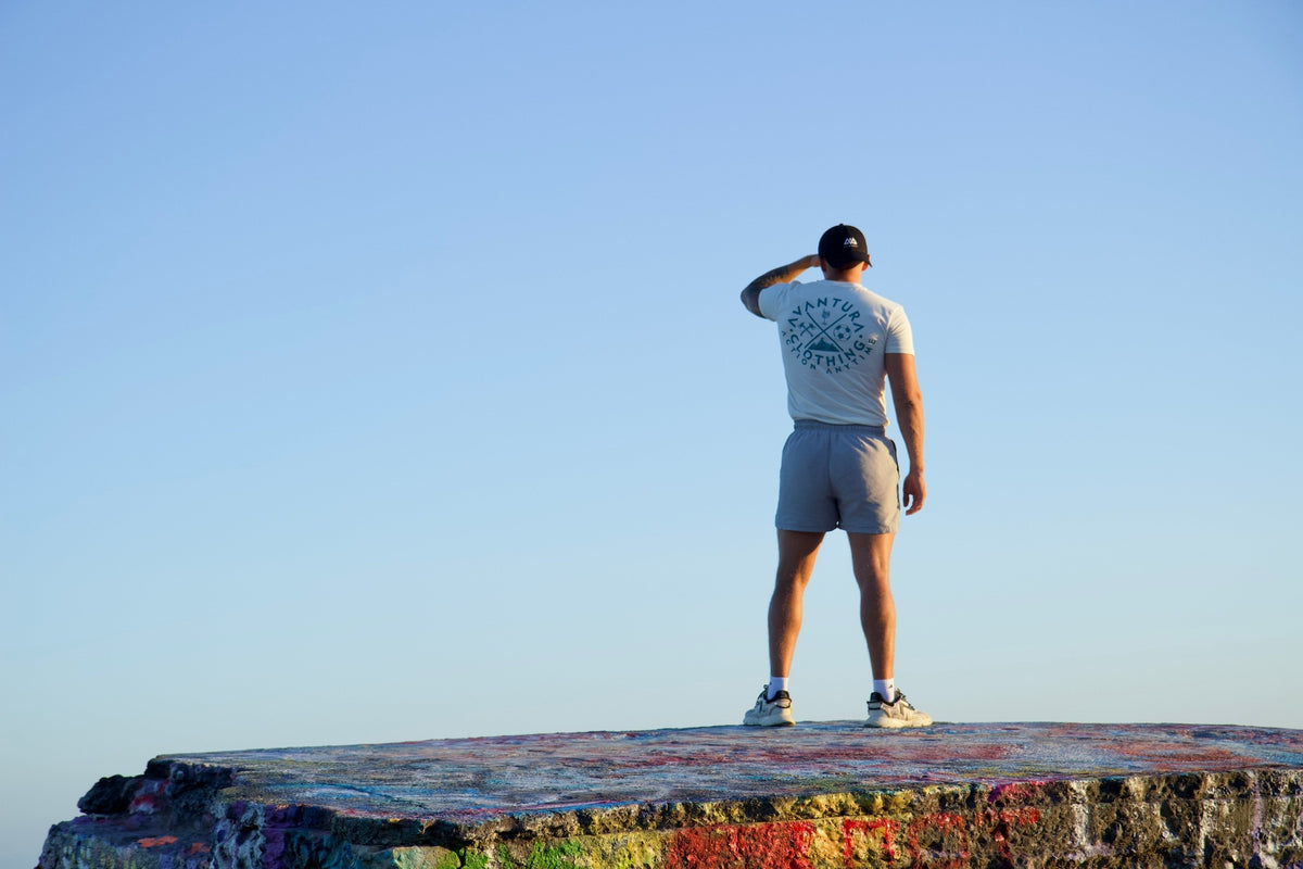 Man in beige t-shirt touching cap brim, showcasing relaxed fit and casual summer style