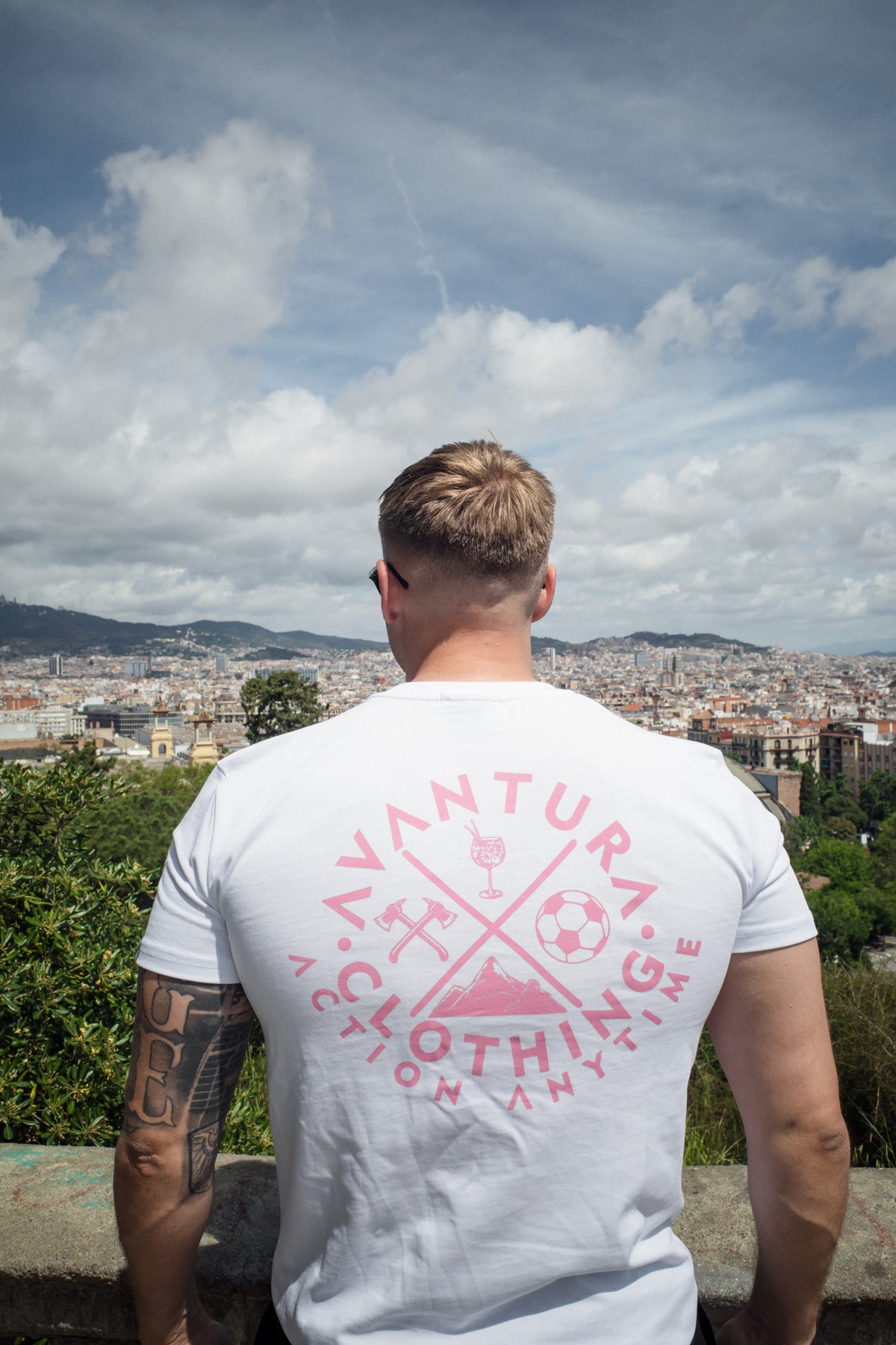 Back view of white t-shirt with large pink emblem print containing four icons