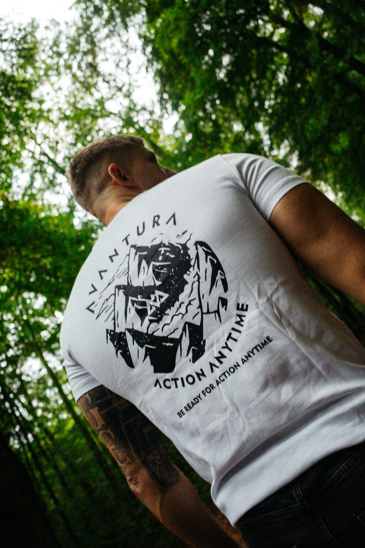 Rückansicht des weißen T-Shirts mit großem Backprint vor grünen Baumkronen
