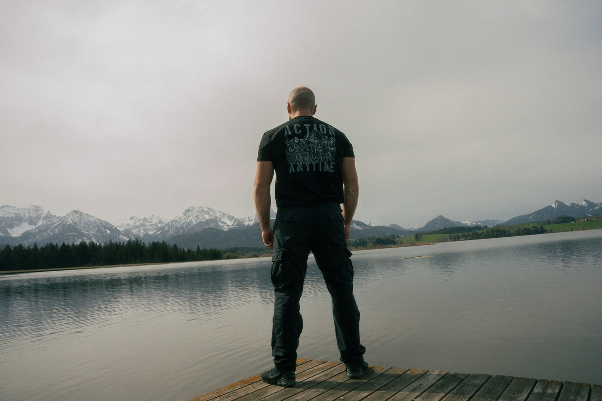 Schwarzes T-Shirt mit ACTION ANYTIME Print vor Bergkulisse