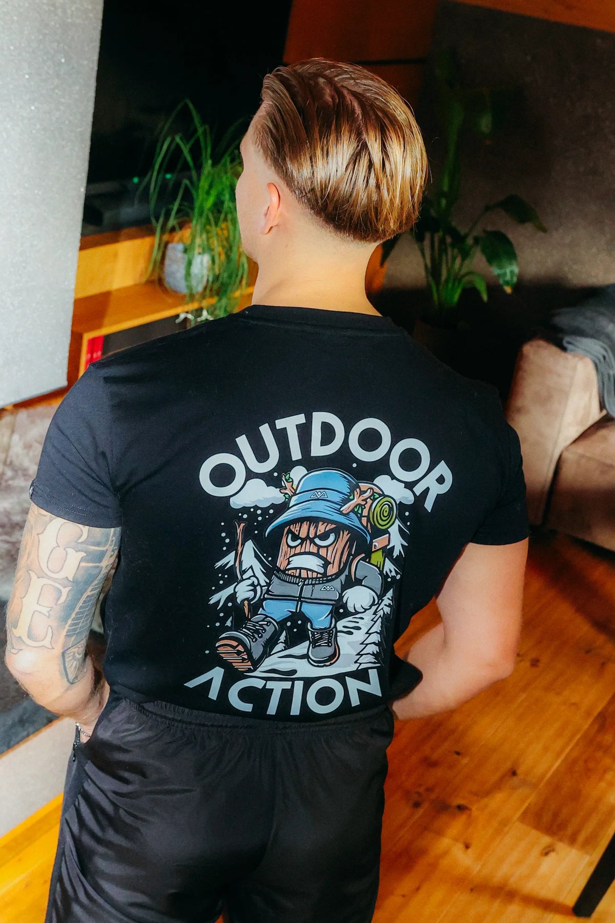 Rear view of black t-shirt with colorful cartoon woodcut character and 'OUTDOOR ACTION' back print