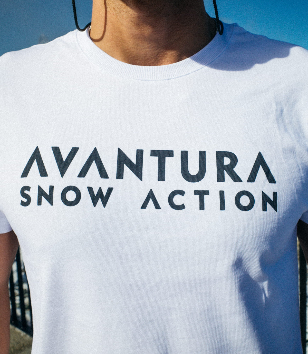 Detailansicht des dunklen AVANTURA SNOW ACTION Logos auf weißem T-Shirt