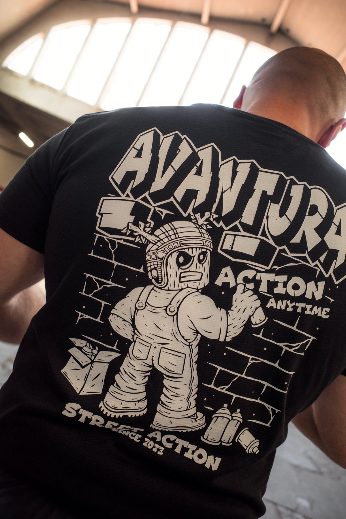 Avantura black T-shirt back print featuring cartoon character and brick wall graphic