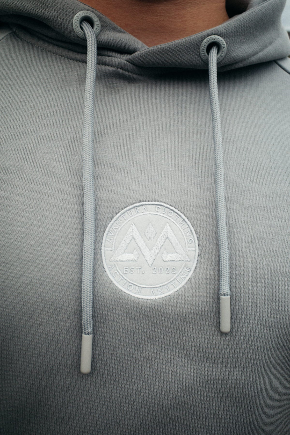 Detail of tonal embroidered logo and drawstrings on the grey hoodie