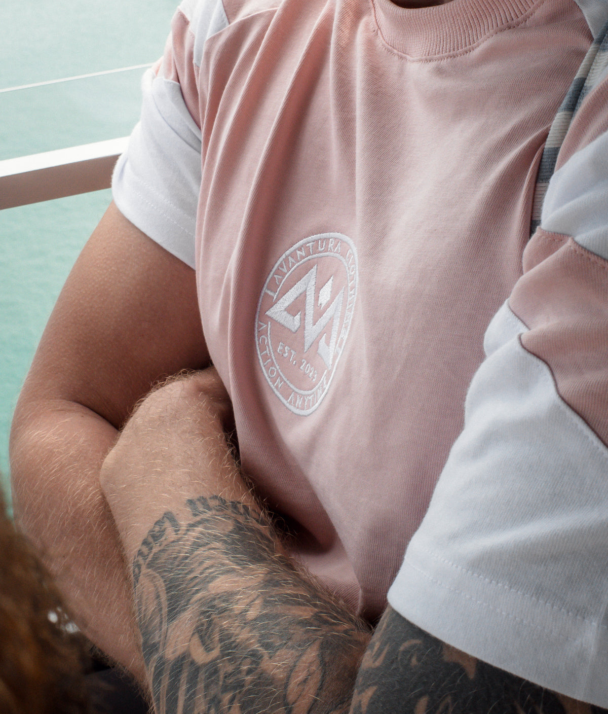 Logo-Stick Detail auf rosa T-Shirt mit sichtbaren Tattoos