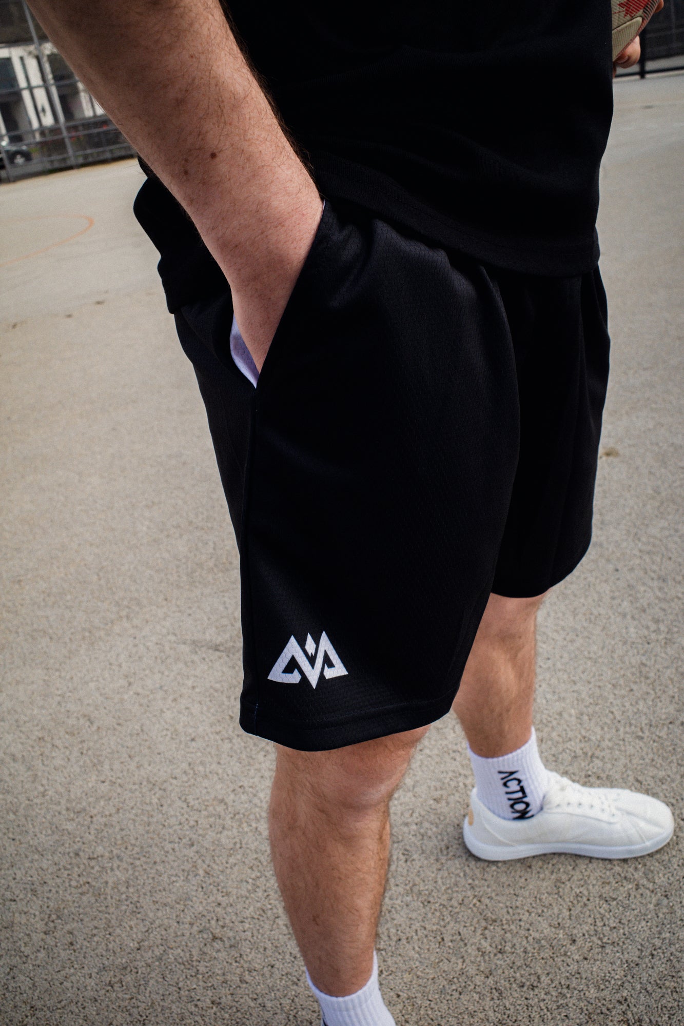 Hand in side pocket of black technical mesh shorts